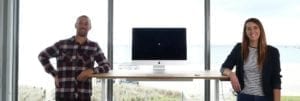 two people leaning on standing desk with mac