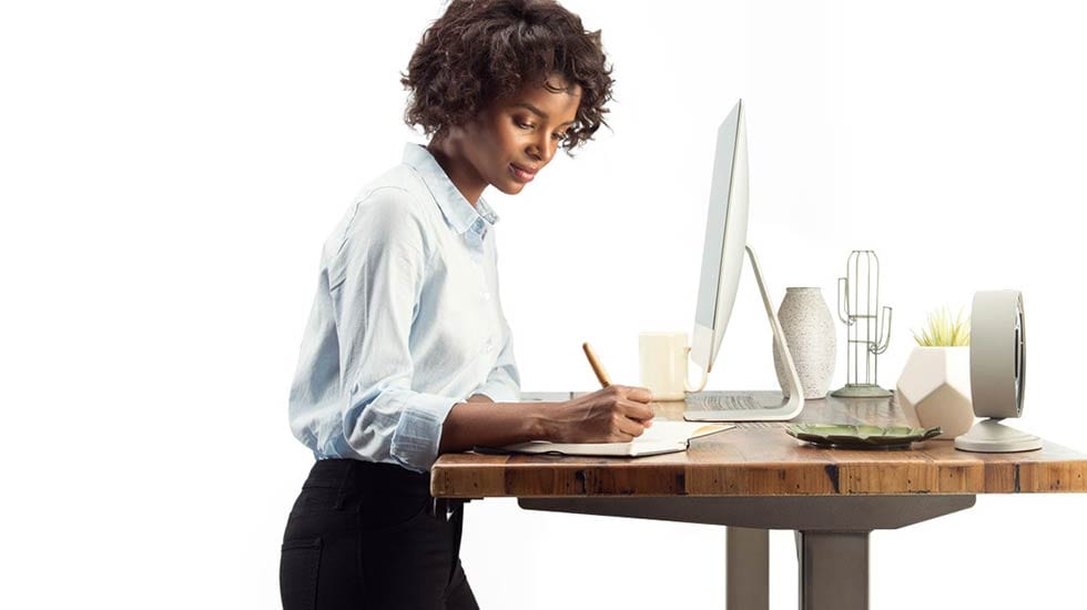 woman writing at brown desk with computer